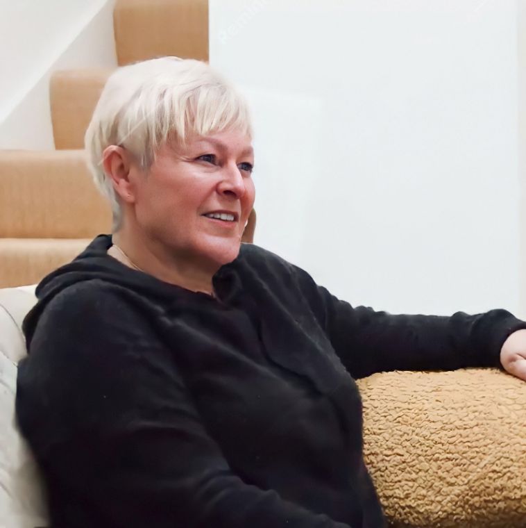 Portrait of jules whale smiling and sitting on her sofa wearing a black hooded top.