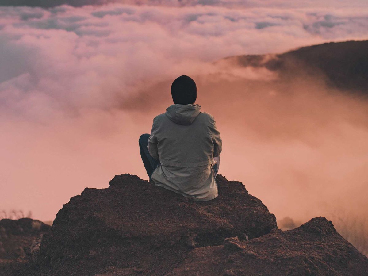 Man looking out into the fog sitting on the edge of a cliff.